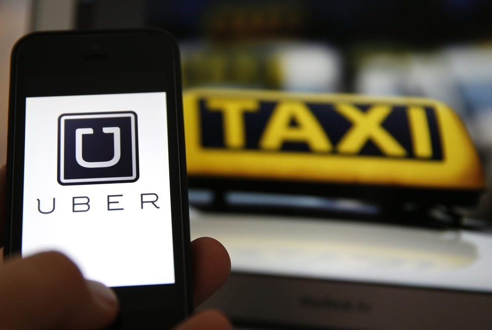 The logo of car-sharing service app Uber on a smartphone next to the picture of an official German taxi sign in Frankfurt, Sept. 15, 2014.