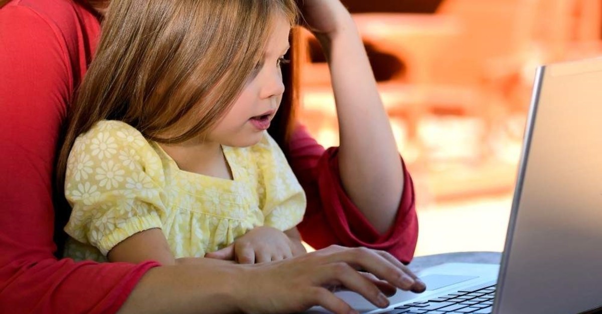 A small girl plays with a computer under the supervision of an adult. (File photo)