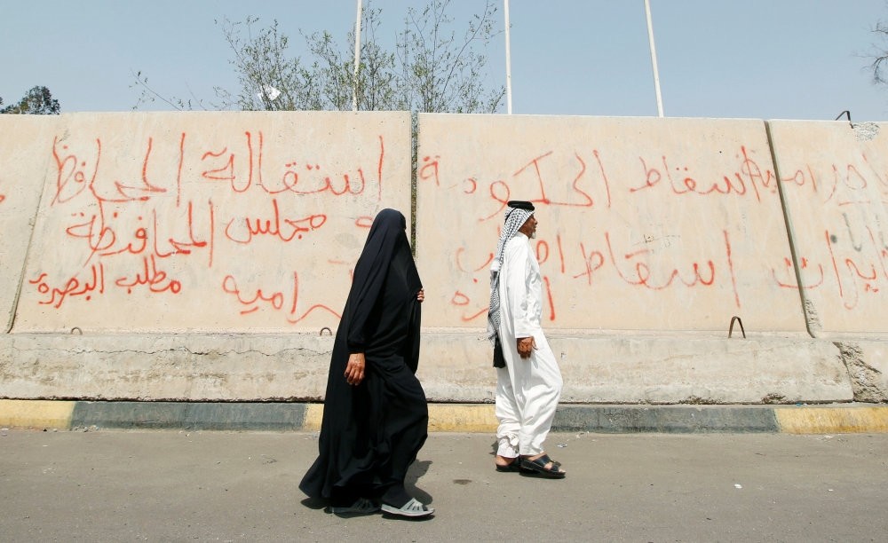 People pass near graffiti painted by protesters after a week of violent protests, Basra, Sept. 9.