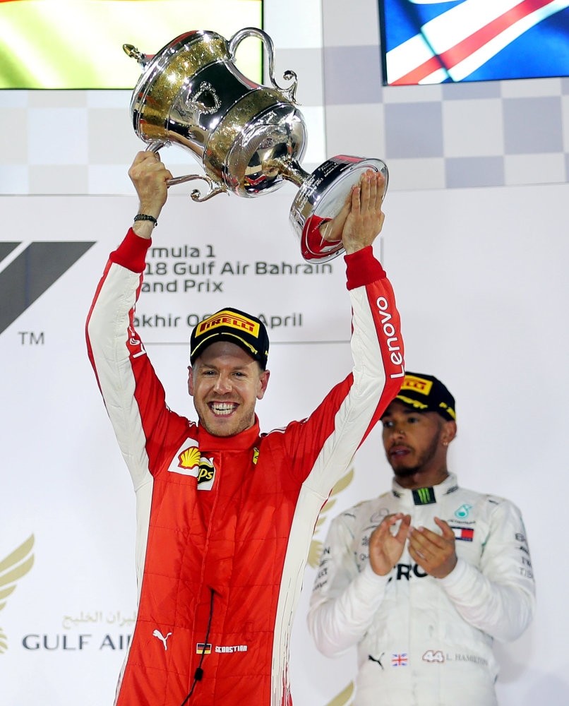 Ferrari's Sebastian Vettel celebrates winning the race with the trophy as Mercedes' Lewis Hamilton looks on.