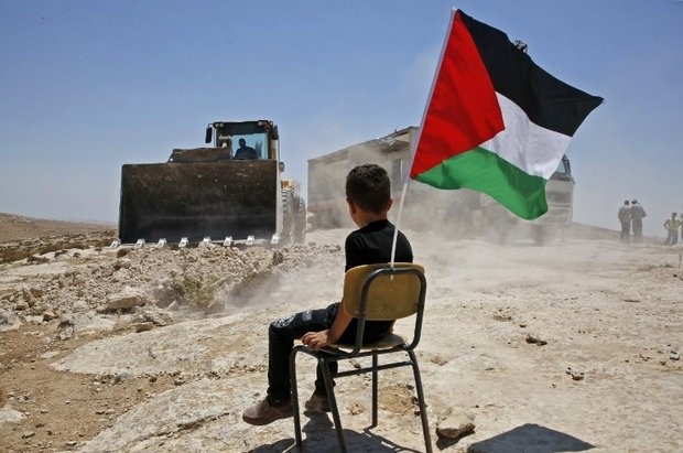 A Palestinian boy sits on a chair with a national flag as Israeli authorities demolish a school site in the village of Yatta, south of the West Bank city of Hebron, July 11.