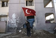 An elderly man waves a Turkish flag in front of a building that was damaged in one of the many PKK/YPG attacks in the region.