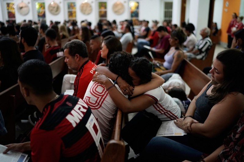 Two young women, wearing Flamengo soccer kits, embrace as they attend a memorial Mass for the victims of a fire at a Brazilian soccer academy, in Rio de Janeiro, Brazil, Friday, Feb. 8, 2019. (AP Photo)