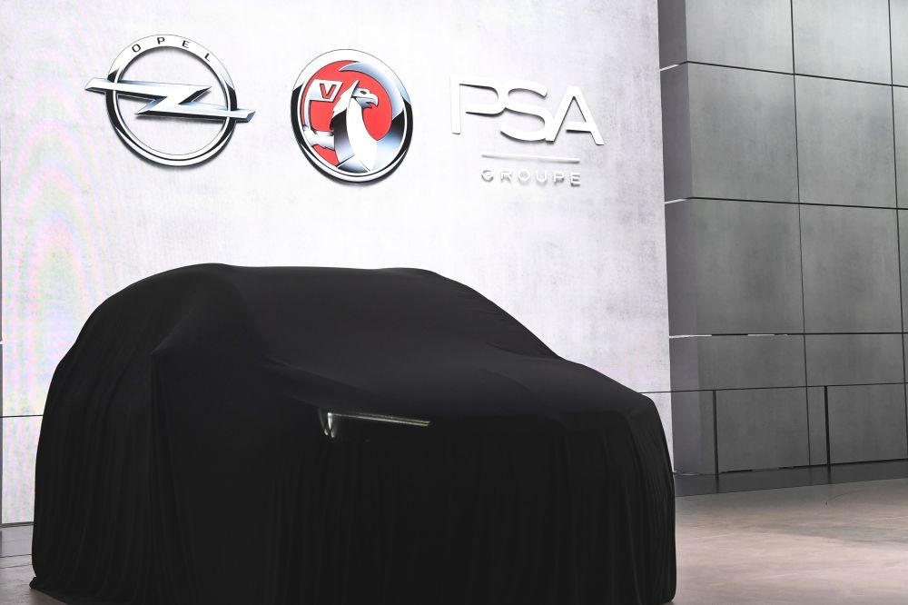Opel, Vauxhall and PSA signs above a covered car during the first press day of the the Geneva International Motor Show in Geneva.
