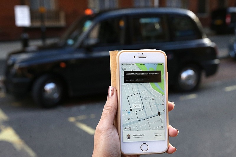 This file photo taken on September 22, 2017 shows a woman posing whilst holding a smartphone showing the App for ride-sharing cab service Uber, near to a black London taxi cab in London. (AFP Photo)