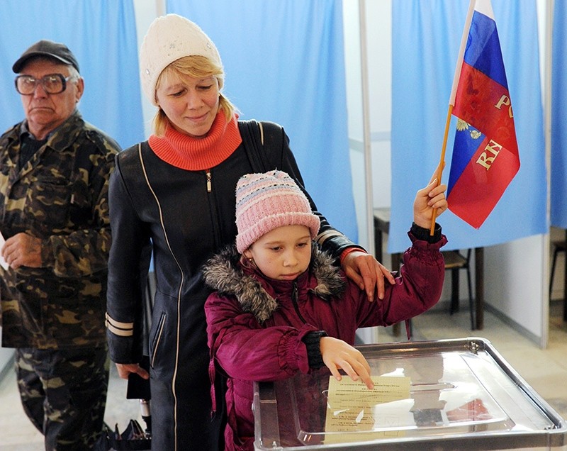 A child casts her mother's ballot while holding a Russian flag at a polling station in Simferopol, Ukraine, March 16, 2014. (AFP Photo)