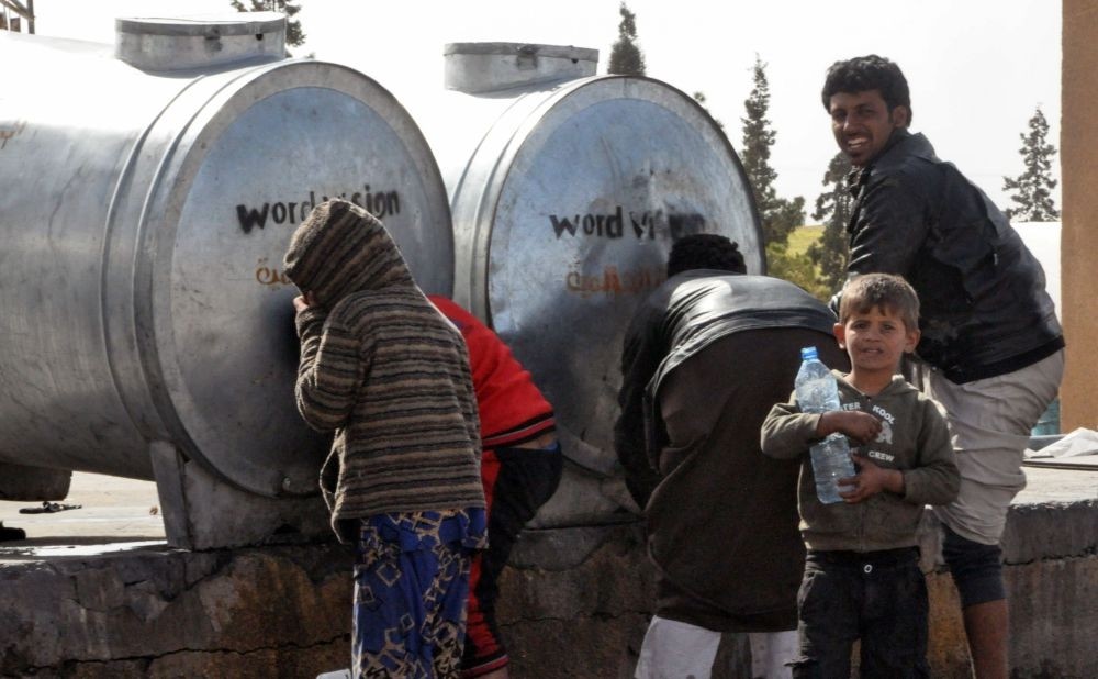 Displaced Syrians, who fled the countryside surrounding Daesh stronghold areas, are drawing water from tanks at a temporary camp in the village of Ain Issa, April 6. (AFP Photo)