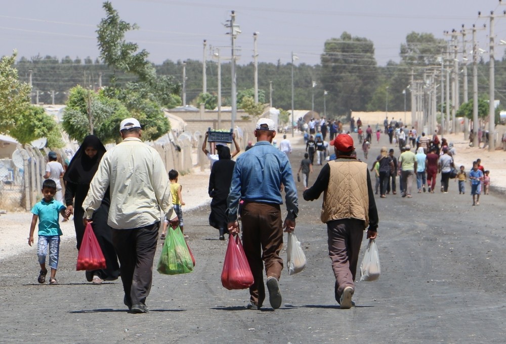 Syrian men carrying grocery bags return to their tents in the refugee camp in Aku00e7akale after traditional Eid shopping.