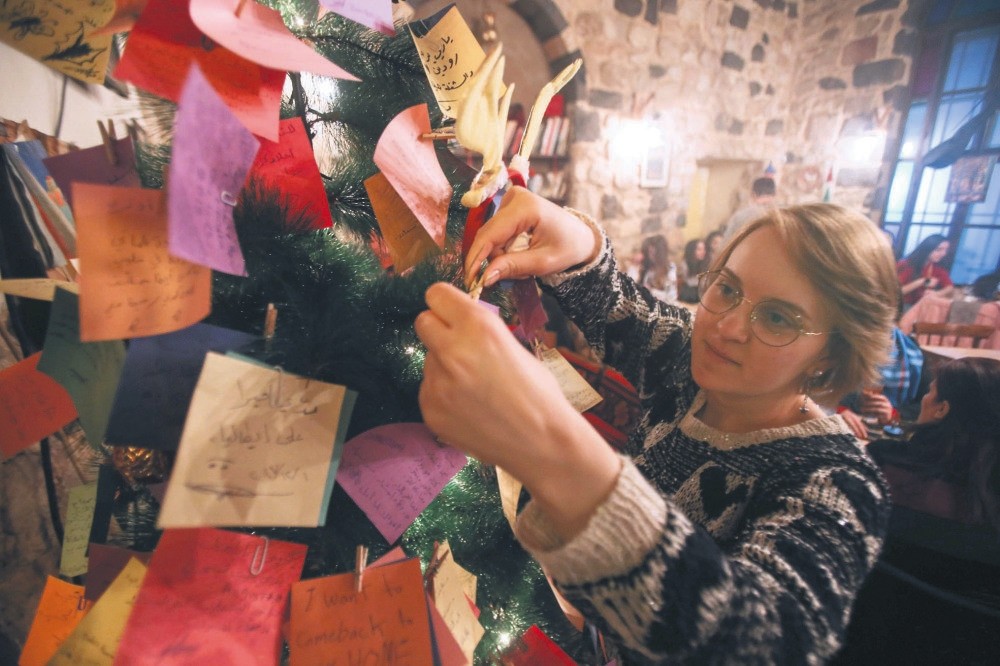 A Syrian youth hangs New Year wishes written on a card on a Christmas tree in the Zeriab coffee shop in the Syrian capital Damascus.