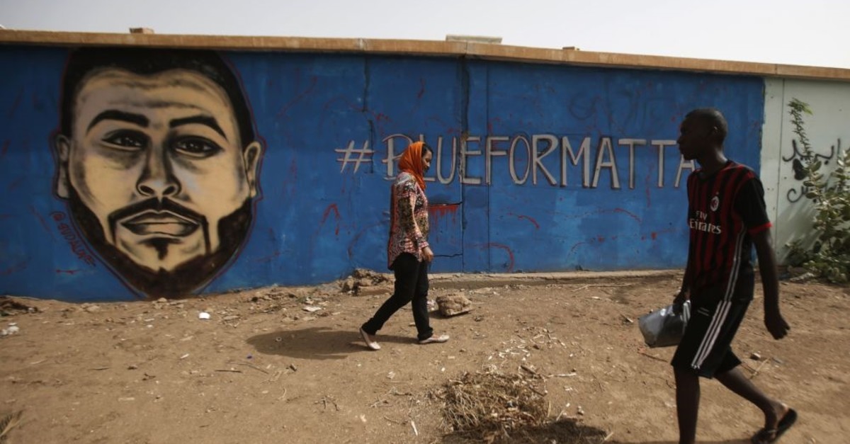 Sudanese artist Asil Diab (L), walks in front of a mural painting of Mohamed Mattar, on the wall of a youth club in Bahri in Khartoum, July 21. Mattar was among dozens killed in the June 3 raid on a protest camp outside the military headquarters.