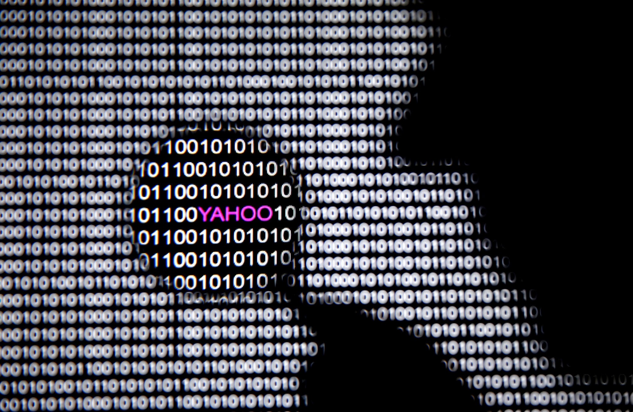 A photo illustration shows a man in front of a Yahoo logo seen through a magnifying glass in front of a displayed cyber code on December 16, 2016. (REUTERS Photo)