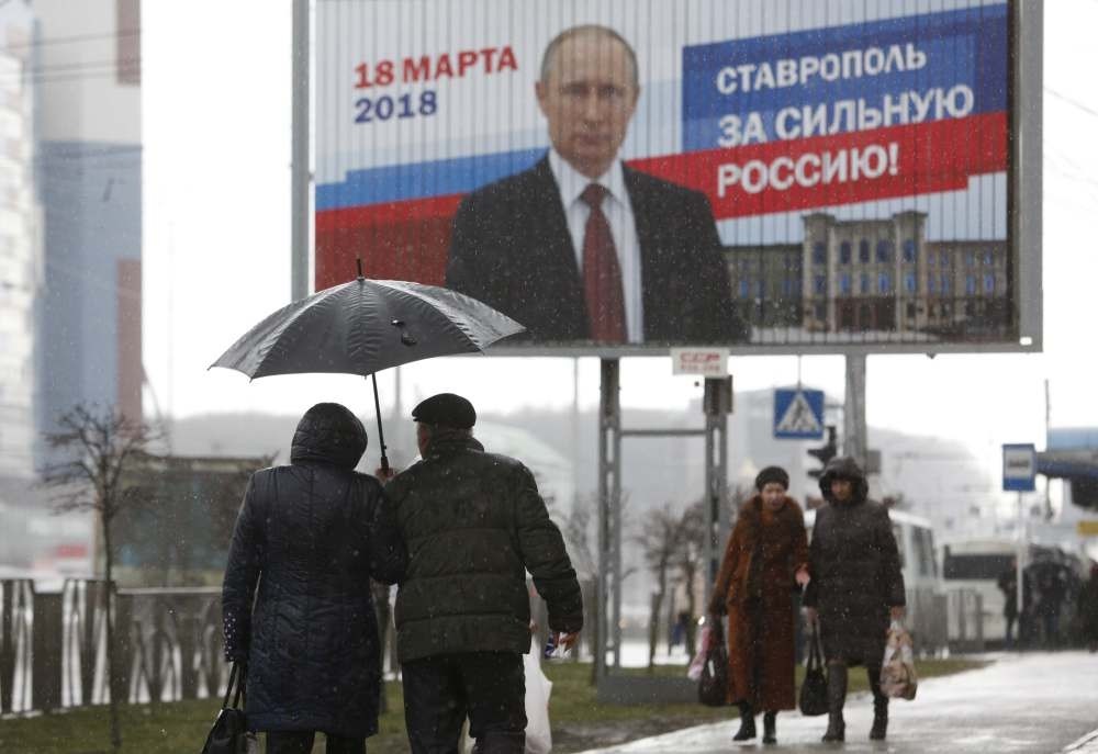People walk past a campaign poster for Russian President Vladimir Putin, Stavropol, Russia, March 14, 2018. The board reads ,Stavropol is for strong Russia!,