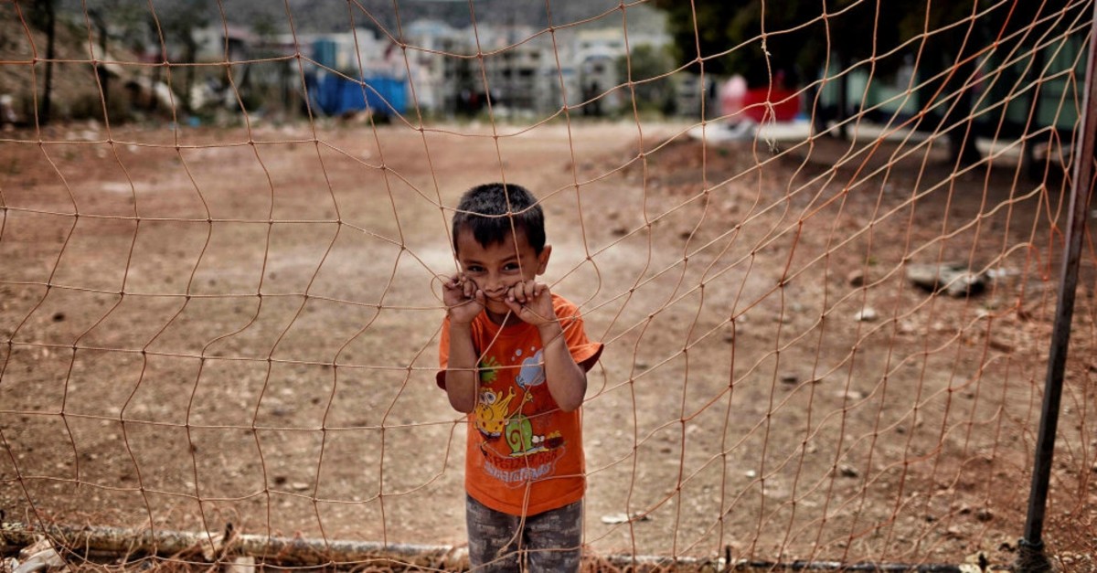 A boy looks on from behind a net at the refugee camp of Schisto, Athens, June 8, 2016.