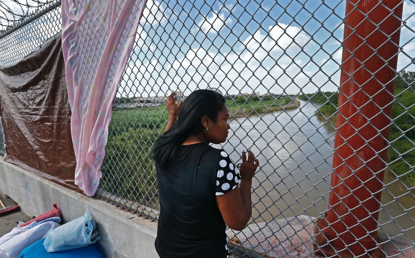 An immigrant seeking asylum looks out across the Rio Grande River while waiting in the middle of the bridge to get into the U.S. from Matamoros, Mexico.