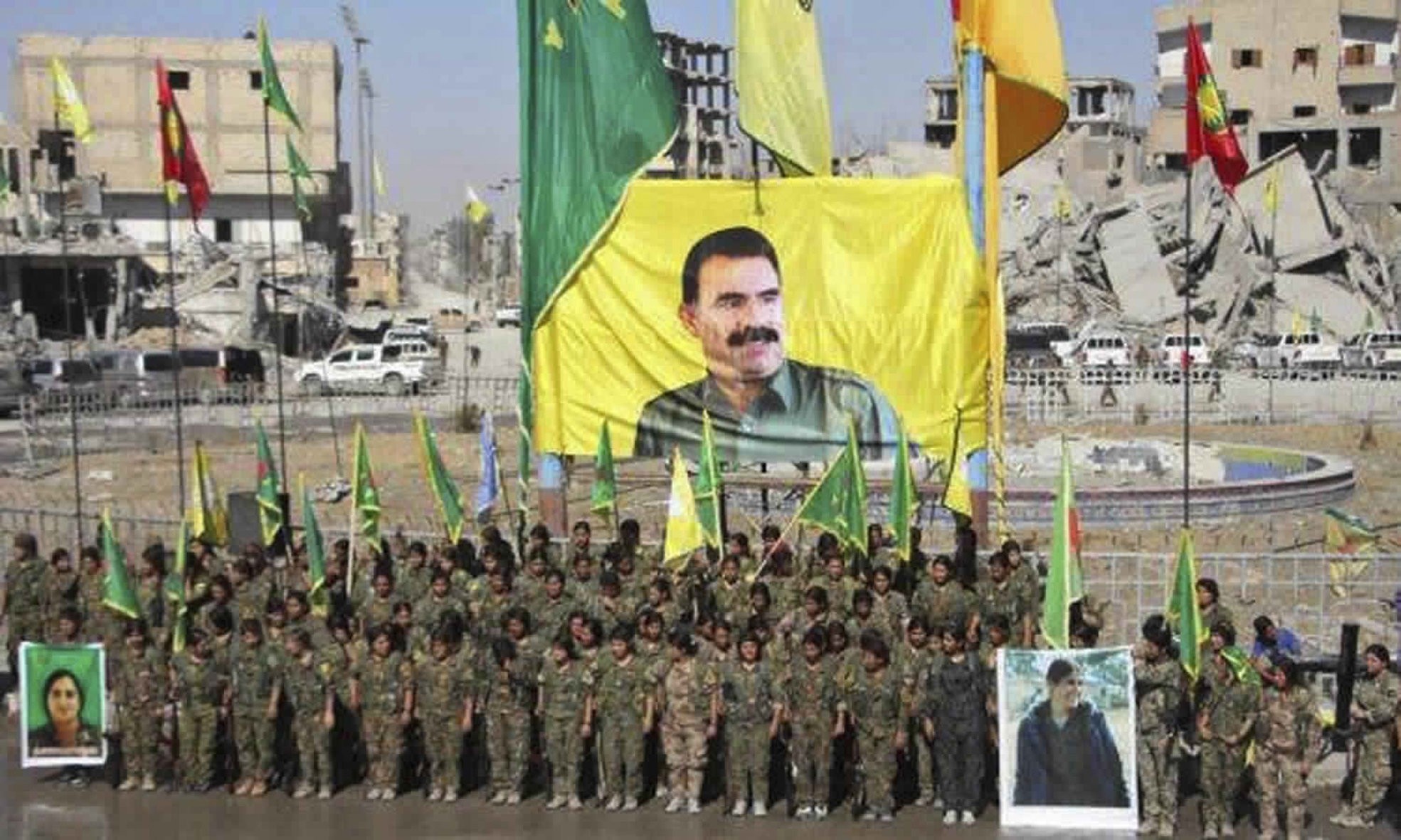YPG members stand under a portrait of their PKK Abdullah Ocalan, as they celebrate victory against Daesh in Raqqa, Syria.(Ronahi TV, via AP)