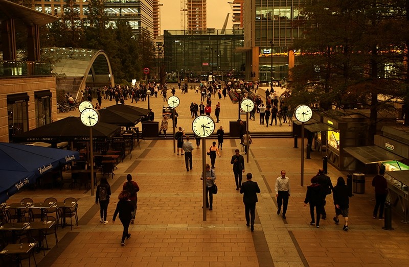 People walk through Canary Wharf while the sky overhead turns red as dust from the Sahara carried by storm Ophelia filters sunlight over London, Britain, October 16, 2017.