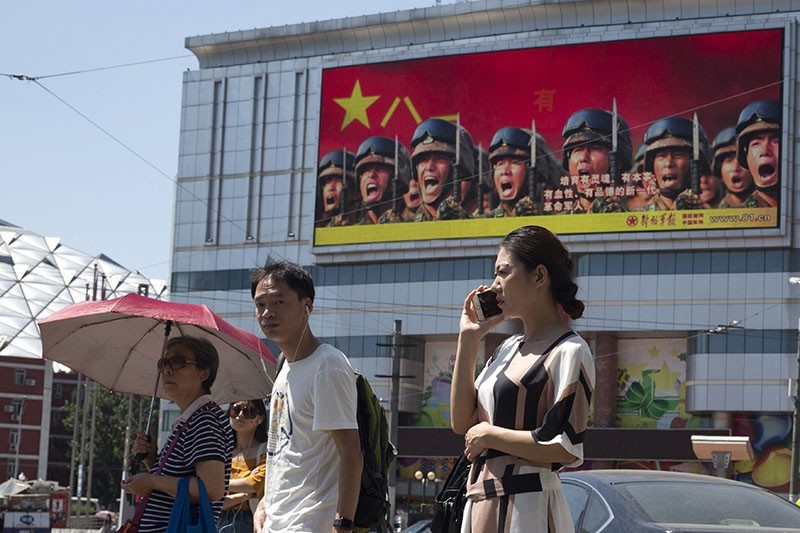 People wait at a traffic junction near a billboard advertising the Chinese military in Beijing, China, Friday, Aug. 4, 2017. (AP Photo)