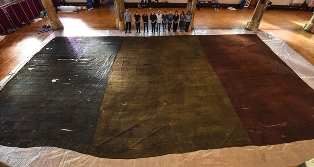 A handout picture released on February 15, 2017 by Norfolk museums service shows curators posing by a giant Tricolour flag at St Andrew’s Hall in Norwich in October 2016. (AFP)
