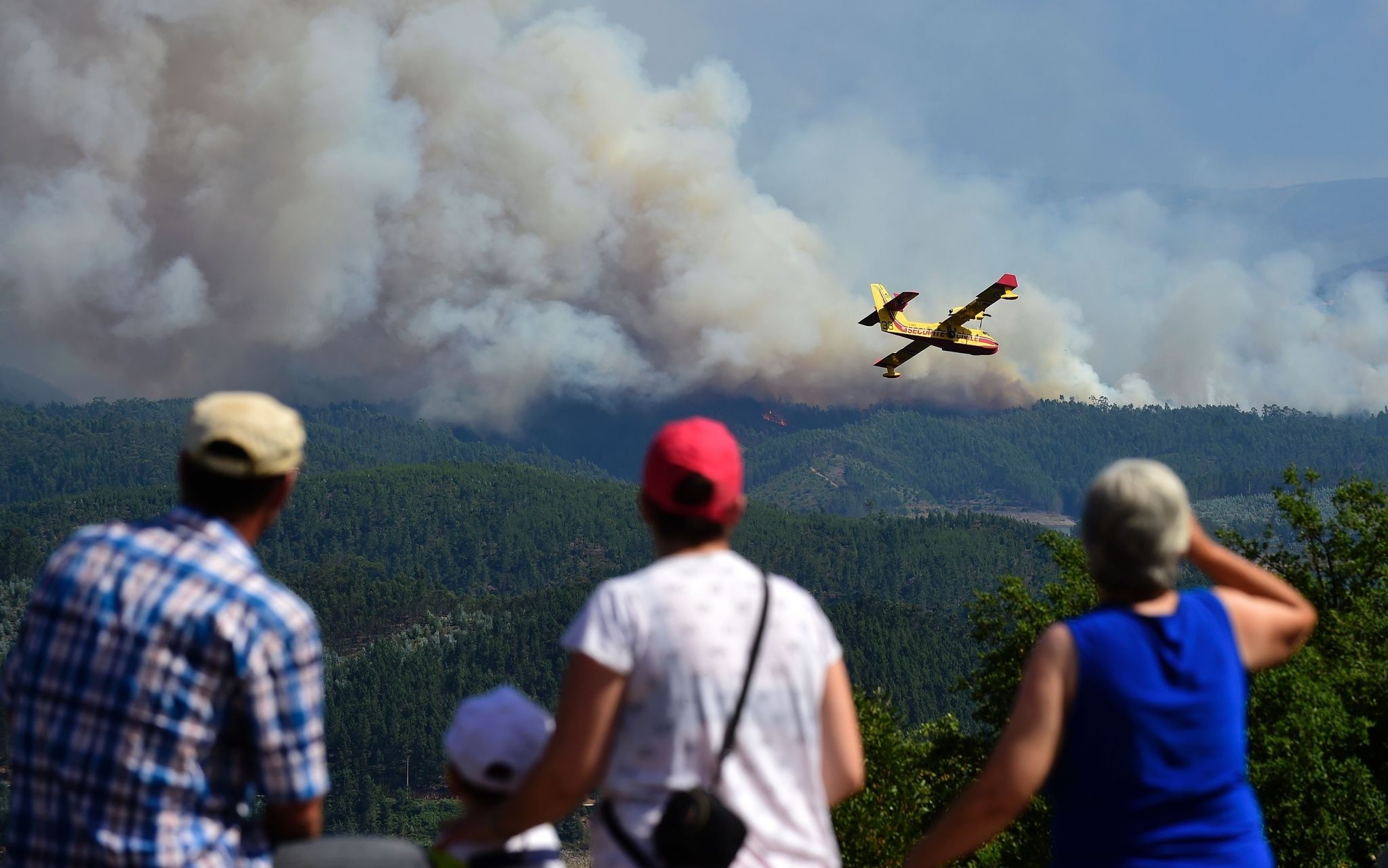 Some locals watch a Canadair plane overflying smoke columns taht raise as wildfires burn close to Pedrogao Pequeno, on June 20, 2017 (AFP Photo)