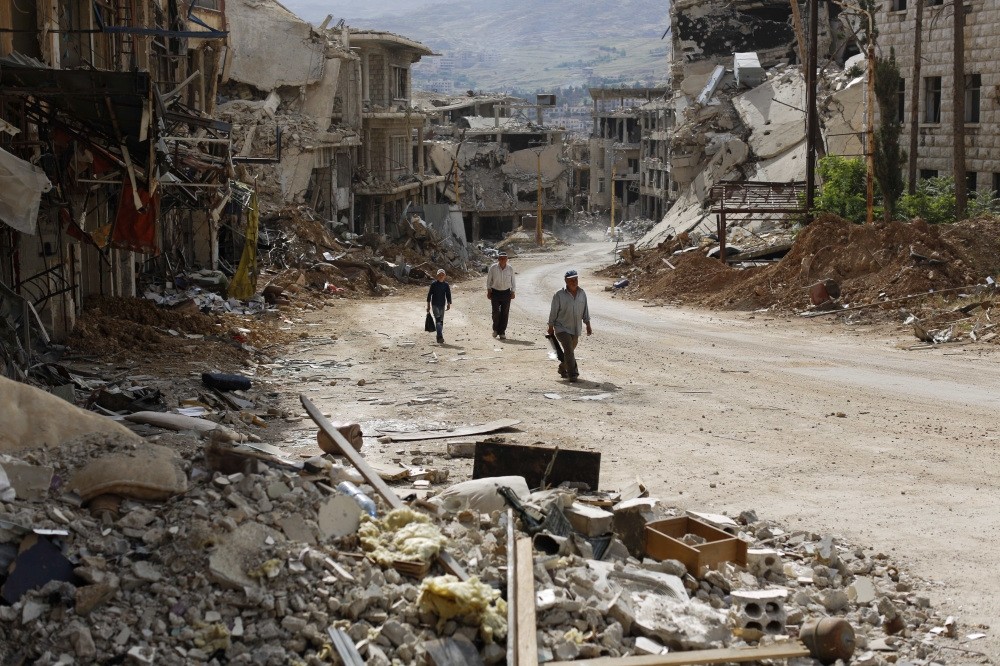 Syrians walk among damaged buildings on a street filled with debri at the mountain resort town of Zabadani in the Damascus countryside, Syria, May 18. 