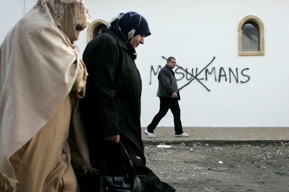 Muslim residents walk past racial slurs painted on the walls of a mosque in the town of Saint-Etienne, central France.