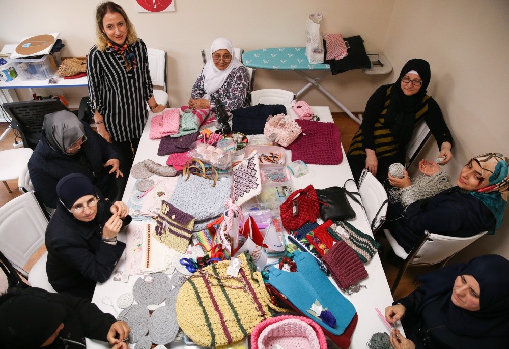 Women sit at a table covered in their handicrafts.