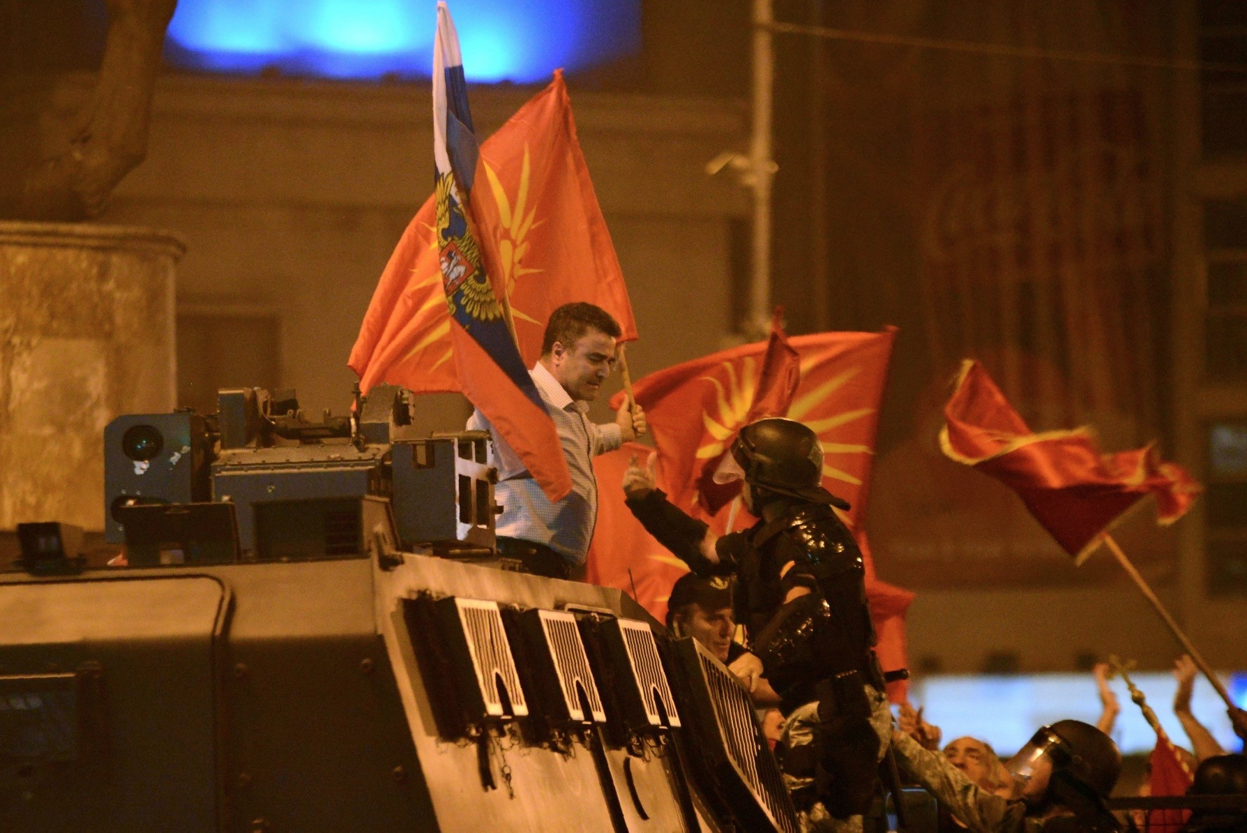 A police officer tries to grab a protester waving former Macedonian and Russian flags atop an armored police vehicle during protests in front of Parliament, Skopje, June 17.