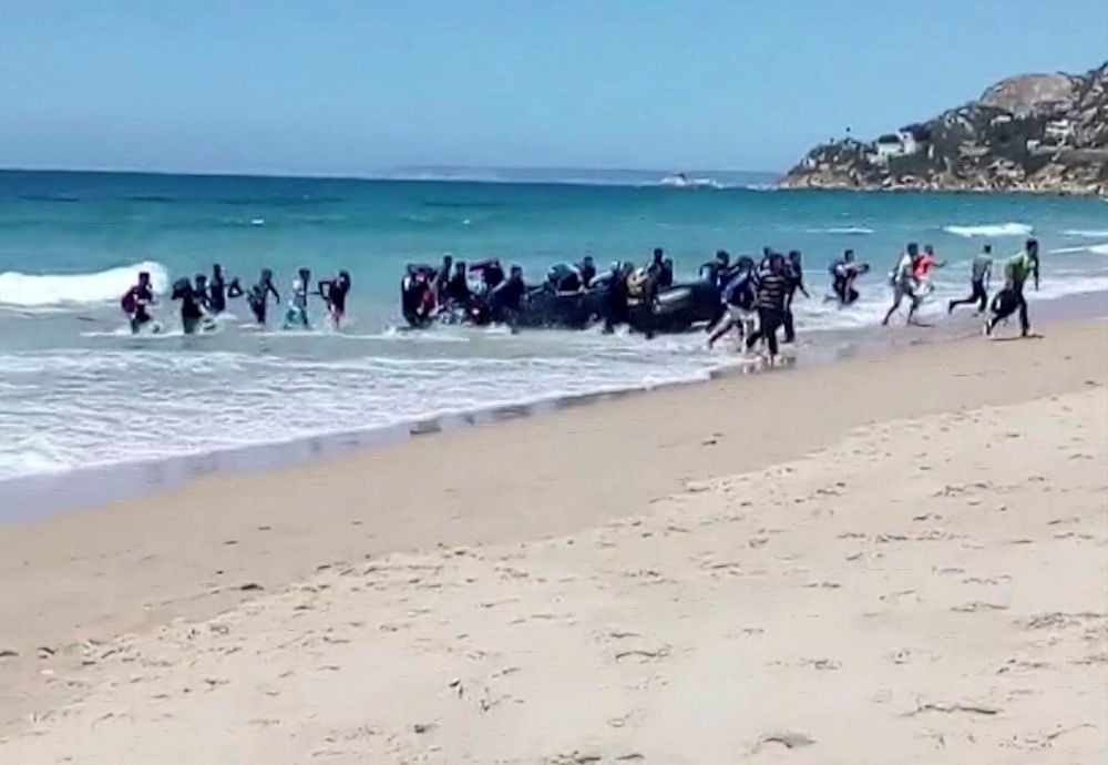 Migrants scatter as a rubber dingy lands on a beach at Cadiz, southern Spain, Aug. 9.