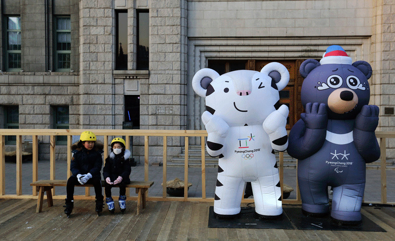 Children sit next to the 2018 Pyeongchang Winter Olympic Games' official mascots, a white tiger Soohorang, for the Olympics, and black bear Bandabi, right, for Paralympics (AP Photo)