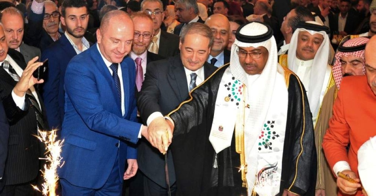 In this Monday, Dec. 2, 2019 photo, the UAE Charge d'affaires Abdul-Hakim Naimi, center right, cuts a cake with Syria's Deputy Foreign Minister Faisal Mekdad (C) to mark UAE's National Day, in Damascus.(SANA via AP)