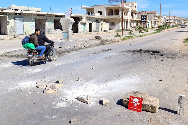 Men ride a motorbike past a hazard sign at a site hit by an airstrike on Tuesday in the town of Khan Sheikhoun in opposition-held Idlib (Reuters Photo)