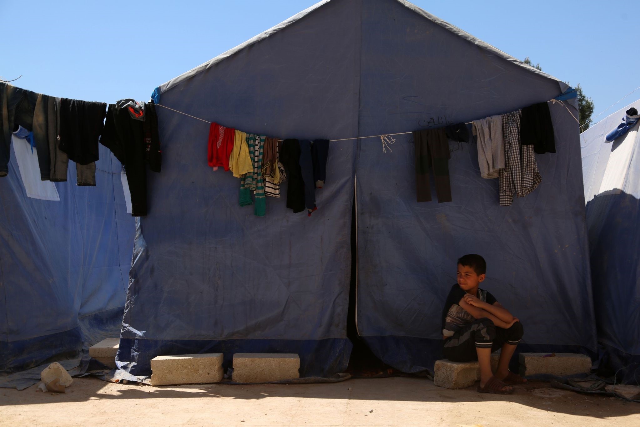 A Syrian boy, displaced from Ghouta following regime chemical weapons attacks, sits outside a tent in a make-shift camp built inside a school in Atareb, northern Syria, April 7.