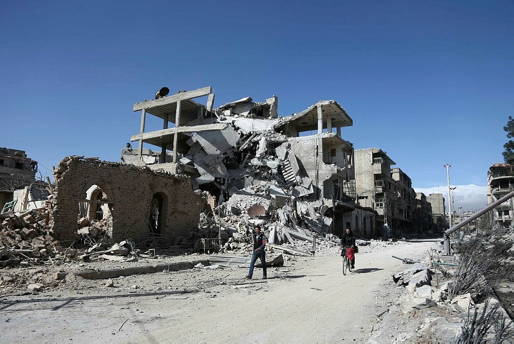 Syrians walk past destroyed buildings in the rebel-held town of Hamouria, in the besieged Eastern Ghouta region on the outskirts of the capital Damascus, on March 9, 2018. (AFP Photo)
