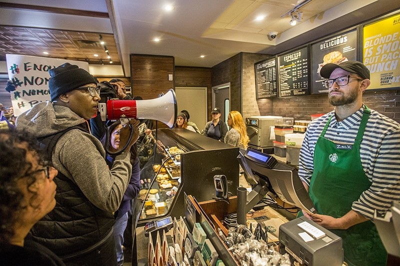 Local Black Lives Matter activist Asa Khalif, left, stands inside a Starbucks, Sunday April 15, 2018, demanding the firing of the manager who called police resulting the arrest of two black men on Thursday (AP Photo)