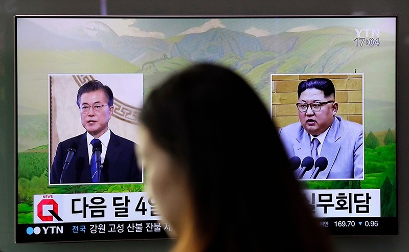 a visitor walks by a TV screen showing file footages of South Korean President Moon Jae-in, left, and North Korean leader Kim Jong Un, right, during a news program at the Seoul Railway Station in Seoul (AP Photo)