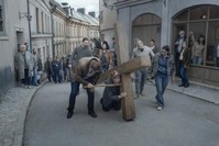 A scene from ,About Endlessness, depicting the priest bearing a huge cross and being tortured by passersby.