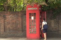 A woman stands near an iconic Red English Telephone booth used as a micro library in Lewisham district of London.