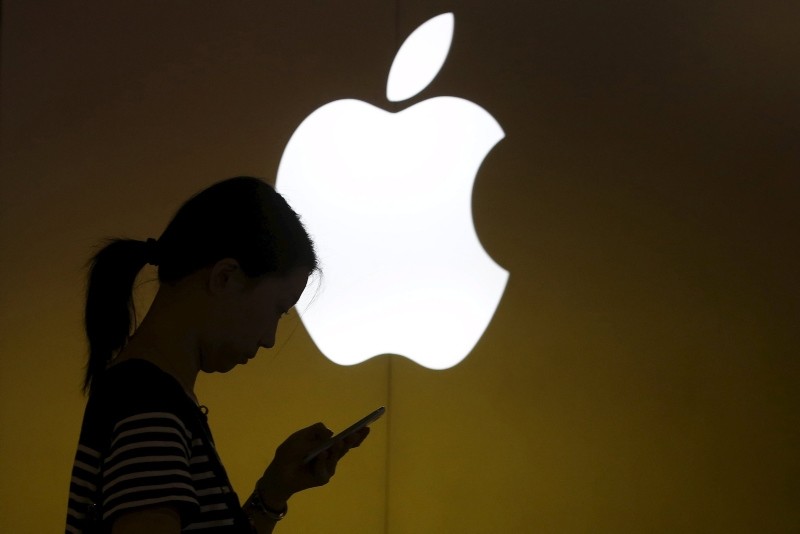 This Sept. 10, 2013 file photo shows a woman looking at the screen of her mobile phone in front of an Apple logo outside its store in downtown Shanghai, China. (Reuters Photo)