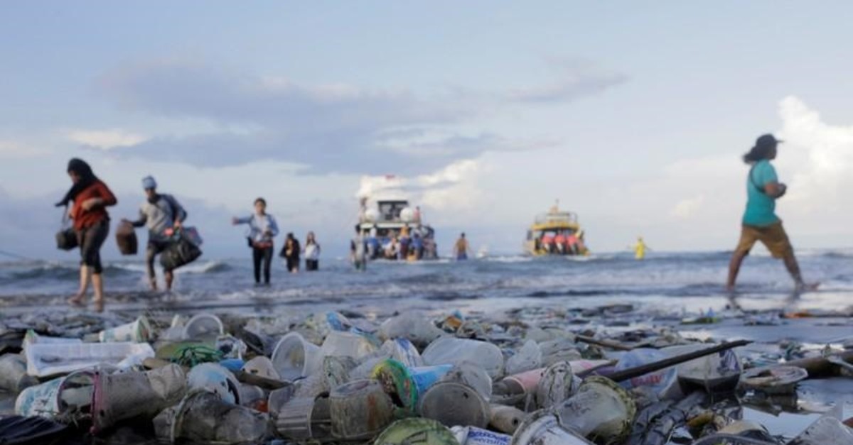 People walk down a beach polluted by plastic waste.  