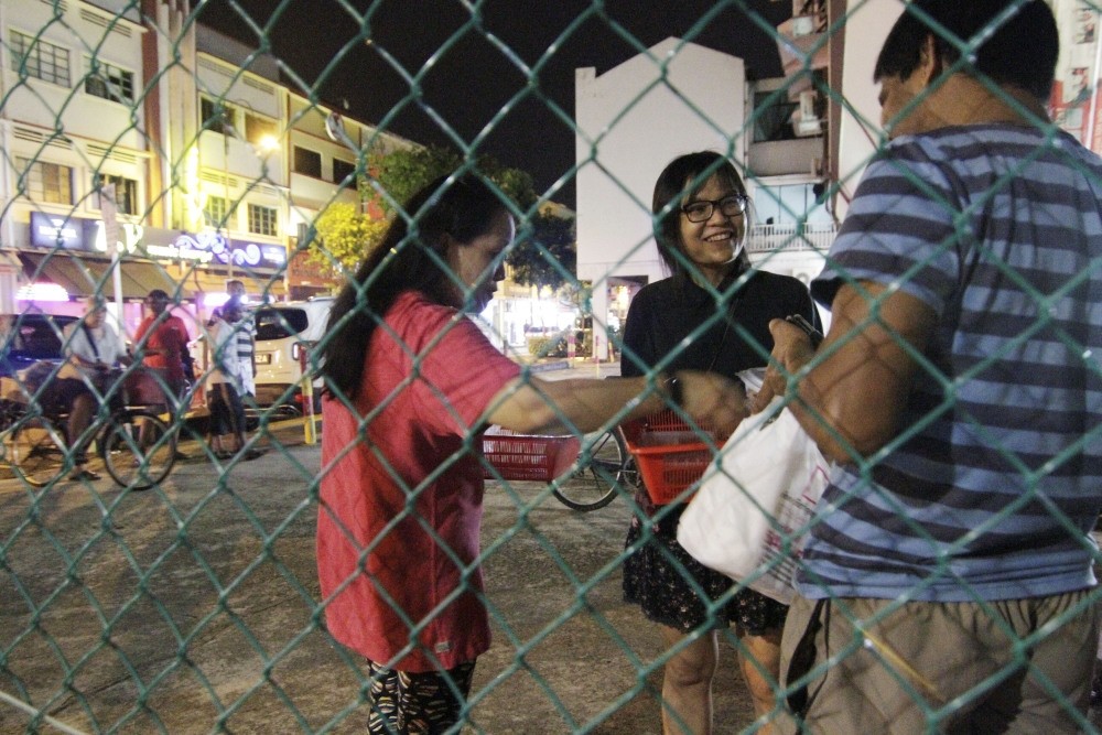 Freegans Joan-ann Chua and Chan Pei Ting give out leftovers to a migrant worker.