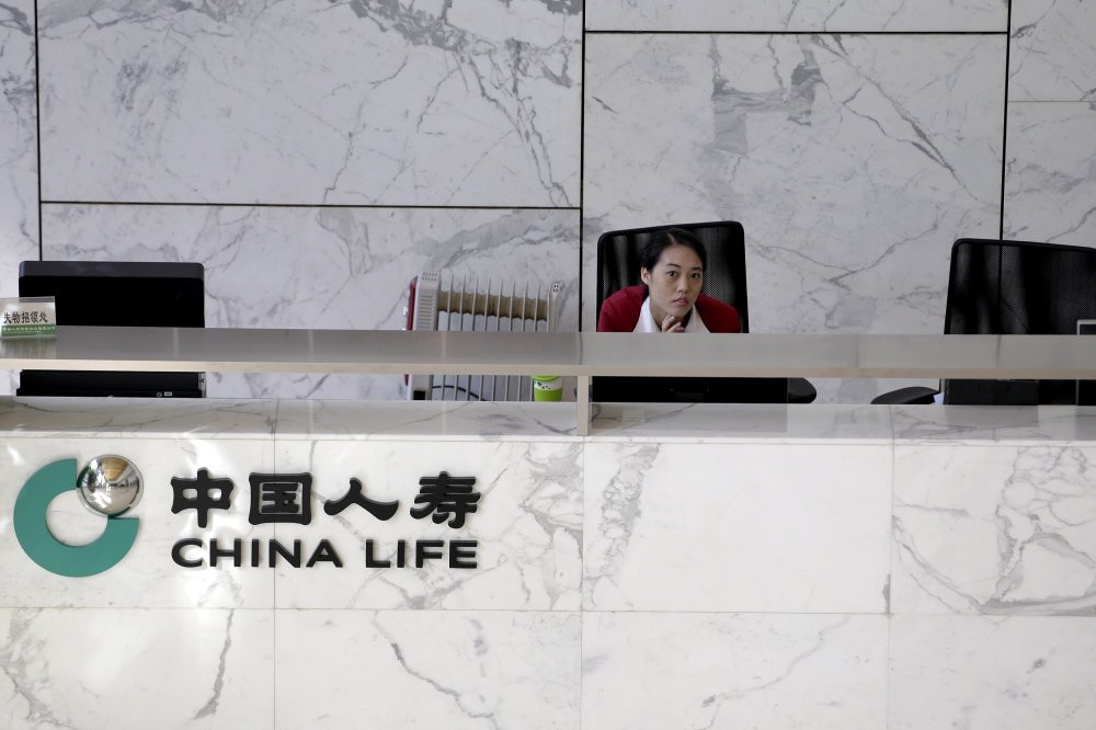 An employee sits at the reception of the headquarters building of China Life insurance in Beijing. China would likely lean on cash-rich SOEs like China Life Insurance to bail out the largest of the struggling companies.