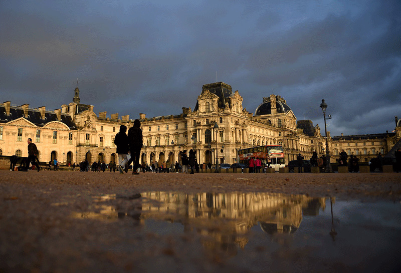Tourists walk past the Richelieu wing of the Louvre Museum under an overcast sky (AFP Photo)