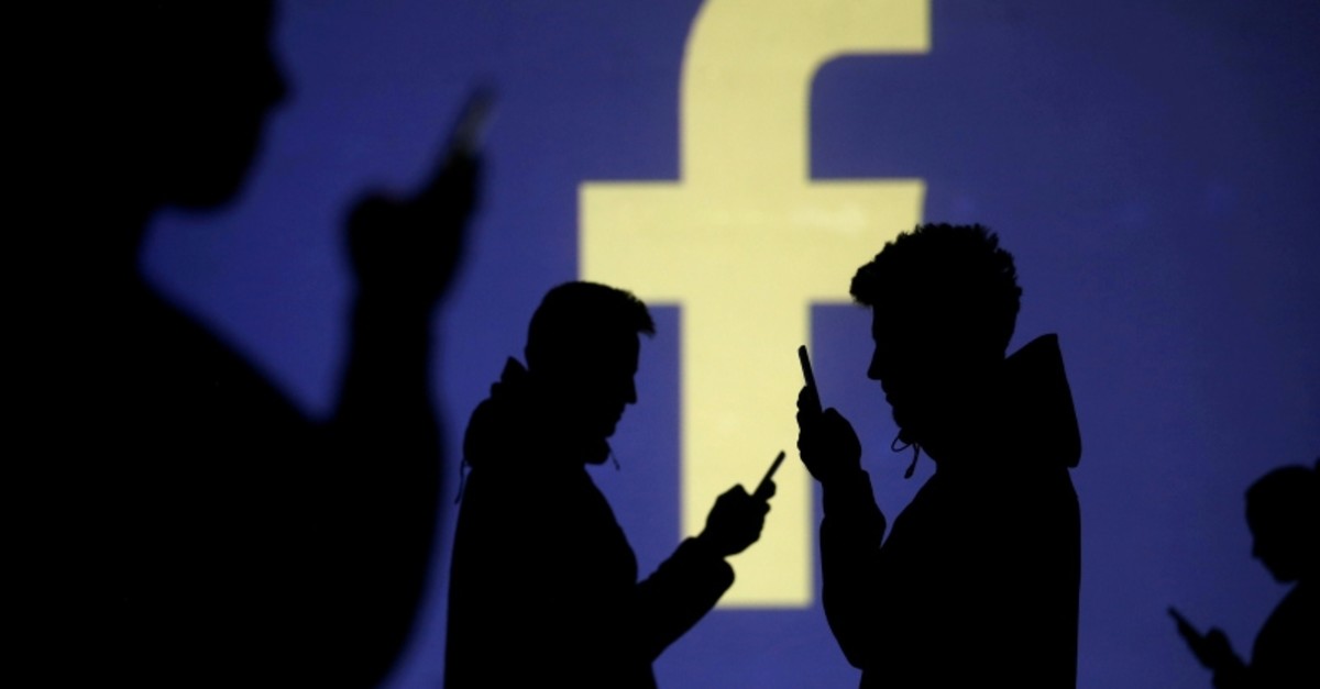 Silhouettes of mobile users are seen next to a screen projection of Facebook logo in this picture illustration taken March 28, 2018. (Reuters Photo)
