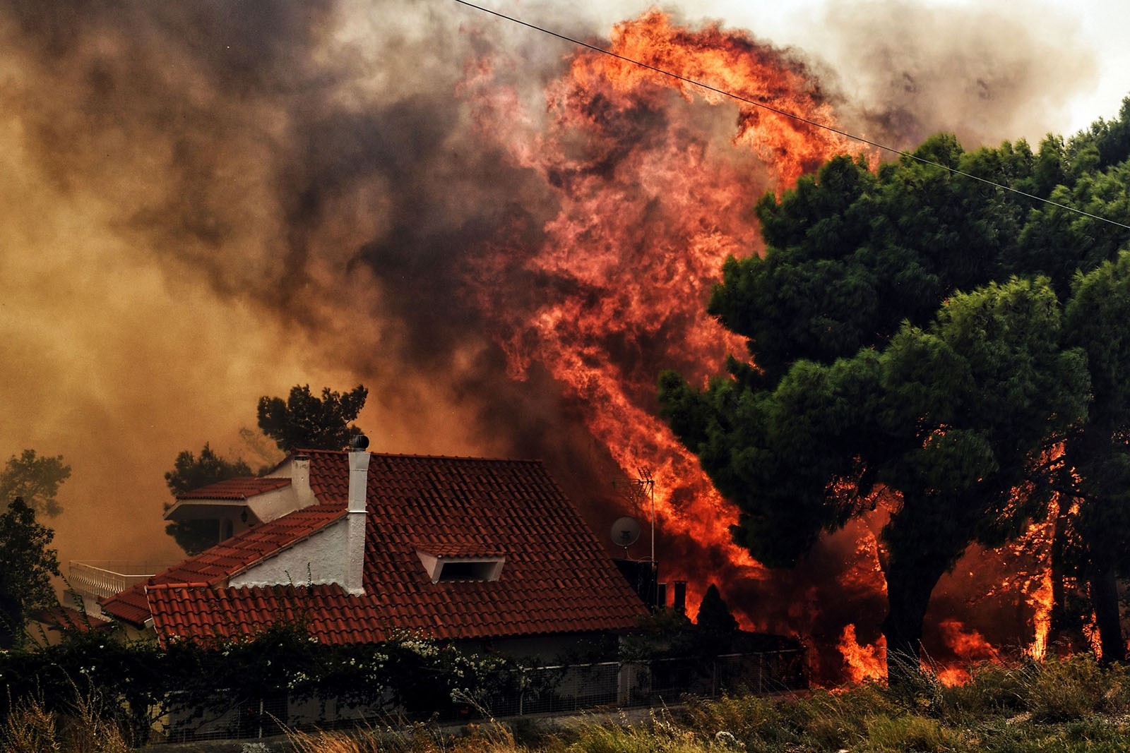 A house is threatened by a huge blaze during a wildfire in Kineta, near Athens, on July 23, 2018.