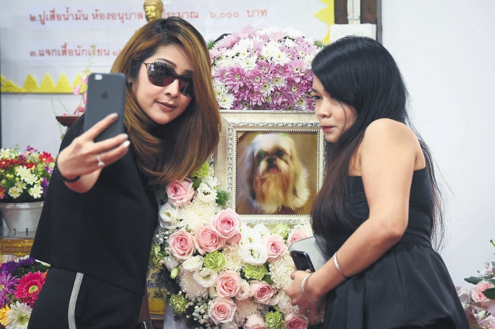 Pimrachaya Worakijmanotham (L) and her friend take a selfie with a photo of Dollar, her six-year-old Shih Tzu, during the pet's funeral.