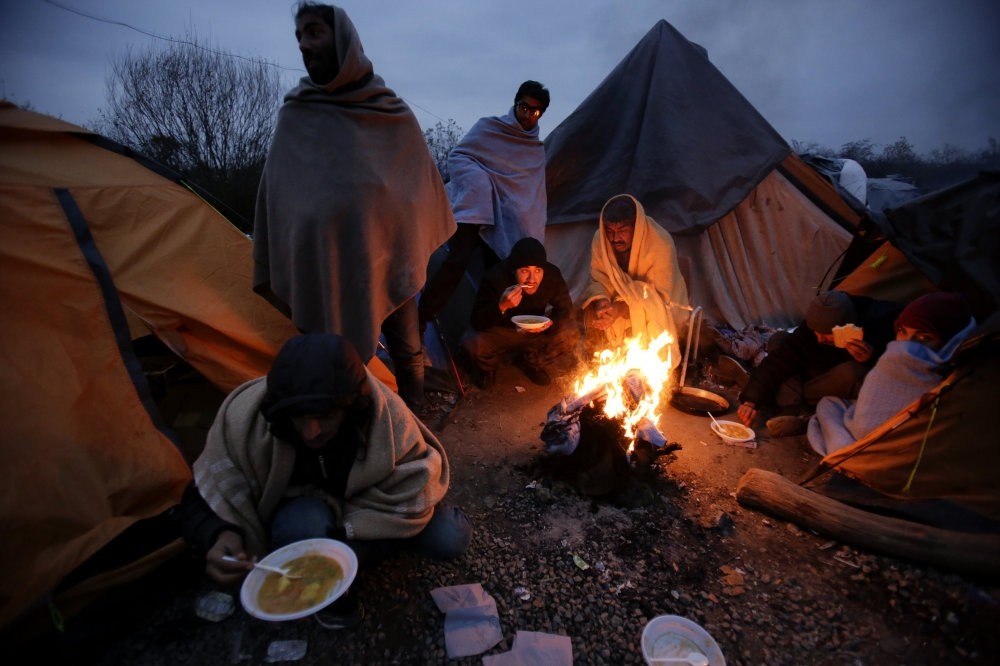 Migrants, seen below eating around a fire at a camp in Velika Kladusa, close to the Croatian border, remain stuck there as winter approaches.