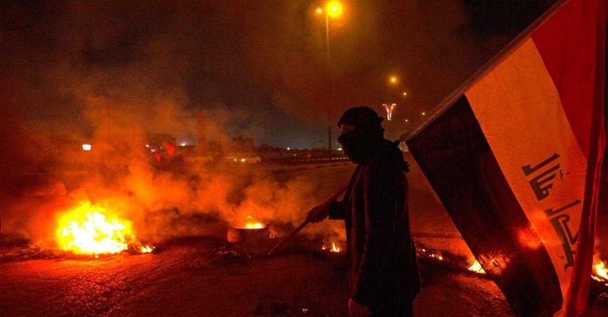 An Iraqi anti-government protester holds the national flag at a roadblock with burning tires, Basra, Dec. 23, 2019. (AFP Photo)