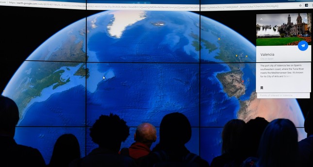 people look at a google earth map on a screen as google earth unveils the revamped