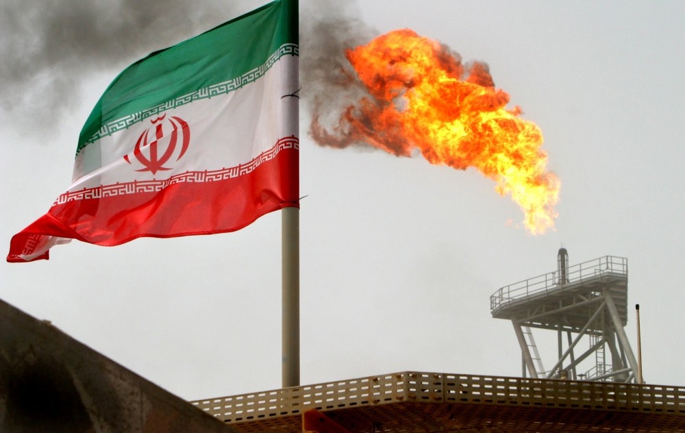 A gas flare on an oil production platform in the Soroush oil fields is seen alongside an Iranian flag in the Persian Gulf.