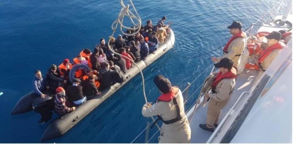 Turkish Coast Guard officials hurls a rope to a boat full of migrants in the Aegean Sea. Migrants pay large sums to smugglers for a spot in packed dinghies.